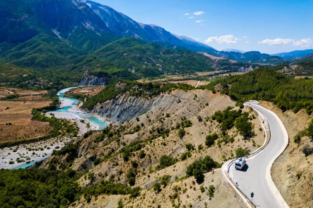 Aerial view of the turquoise Vjosa River winding through a mountain valley in Albania, with a curving road along the ridge