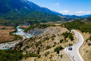 Aerial view of the turquoise Vjosa River winding through a mountain valley in Albania, with a curving road along the ridge