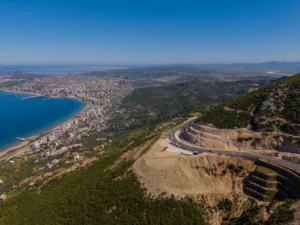 Aerial view of Vlorë, Albania, showing the coastal city along the bay with a winding mountain road in the foreground