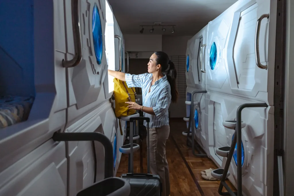 A solo traveler settles into her pod at a capsule hostel, luggage beside her